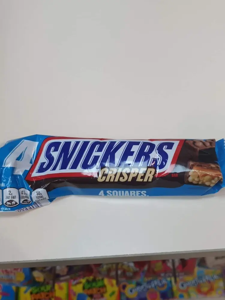 A Snickers Crisper 4-square bar held above a shelf of sour sweets
